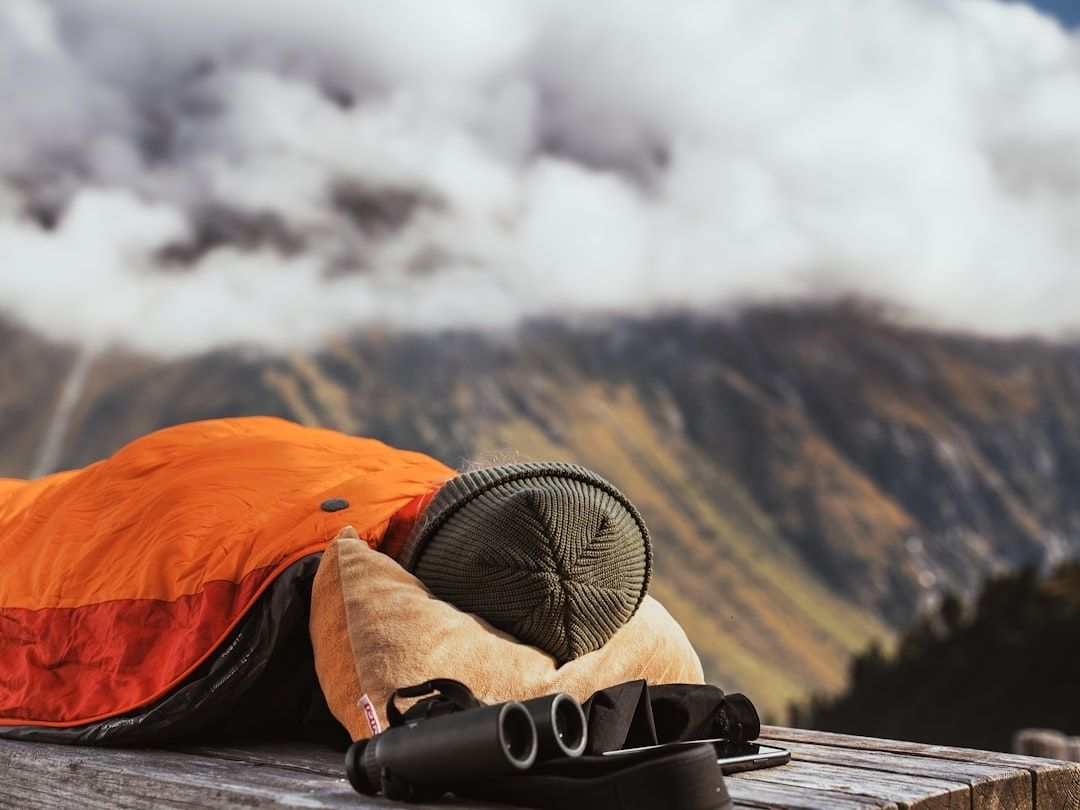 Sac de couchage orange et jumelles posés devant des montagnes