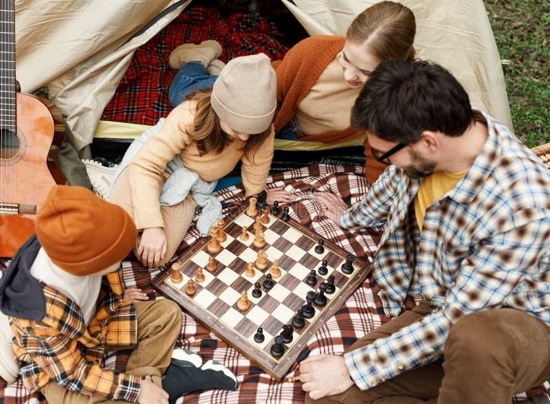 Quatre personnes jouent aux échecs devant une tente de camping