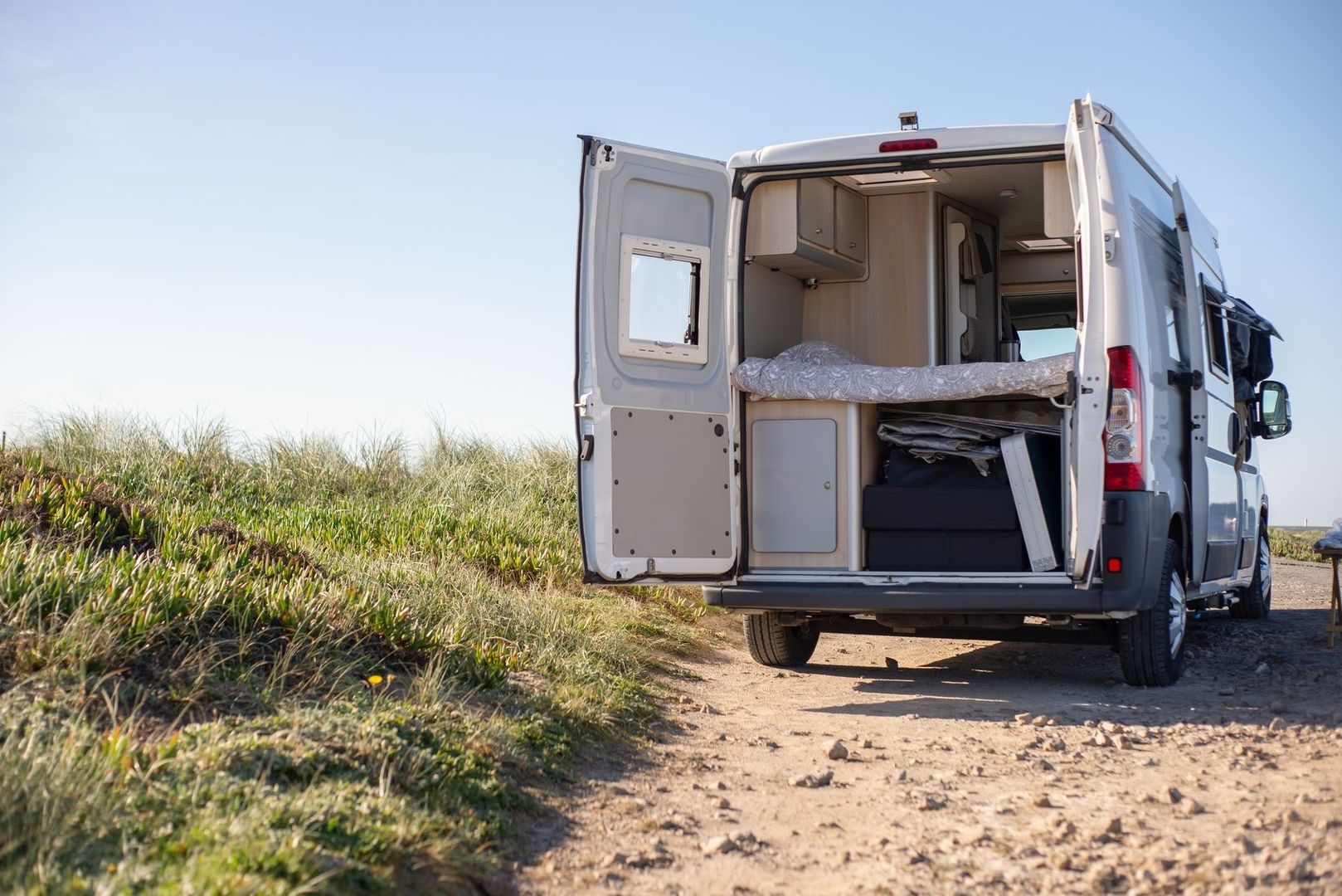 Van aménagé ouvert sur un chemin côtier, avec couchage visible